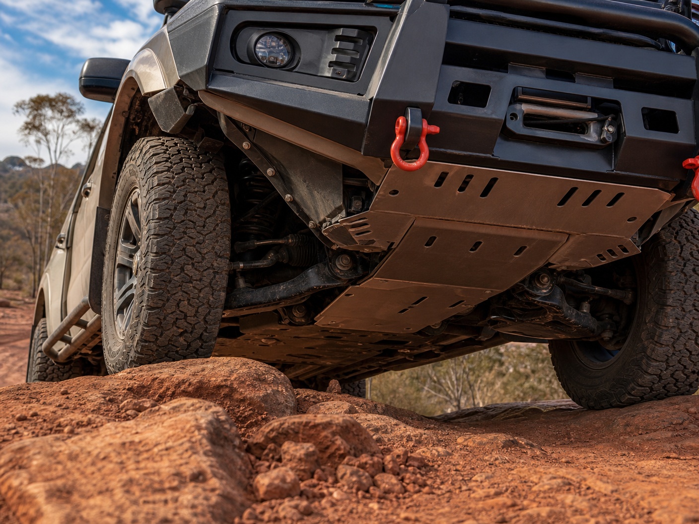 Brand-free low angle view of 4x4 underbody bash plates skid plates and red recovery point on rocky terrain