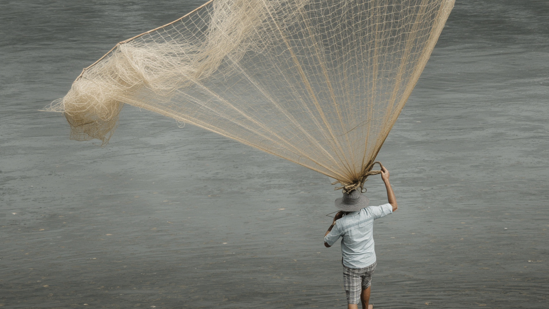 A cast net fanning out into a circle over shallow water at first light.