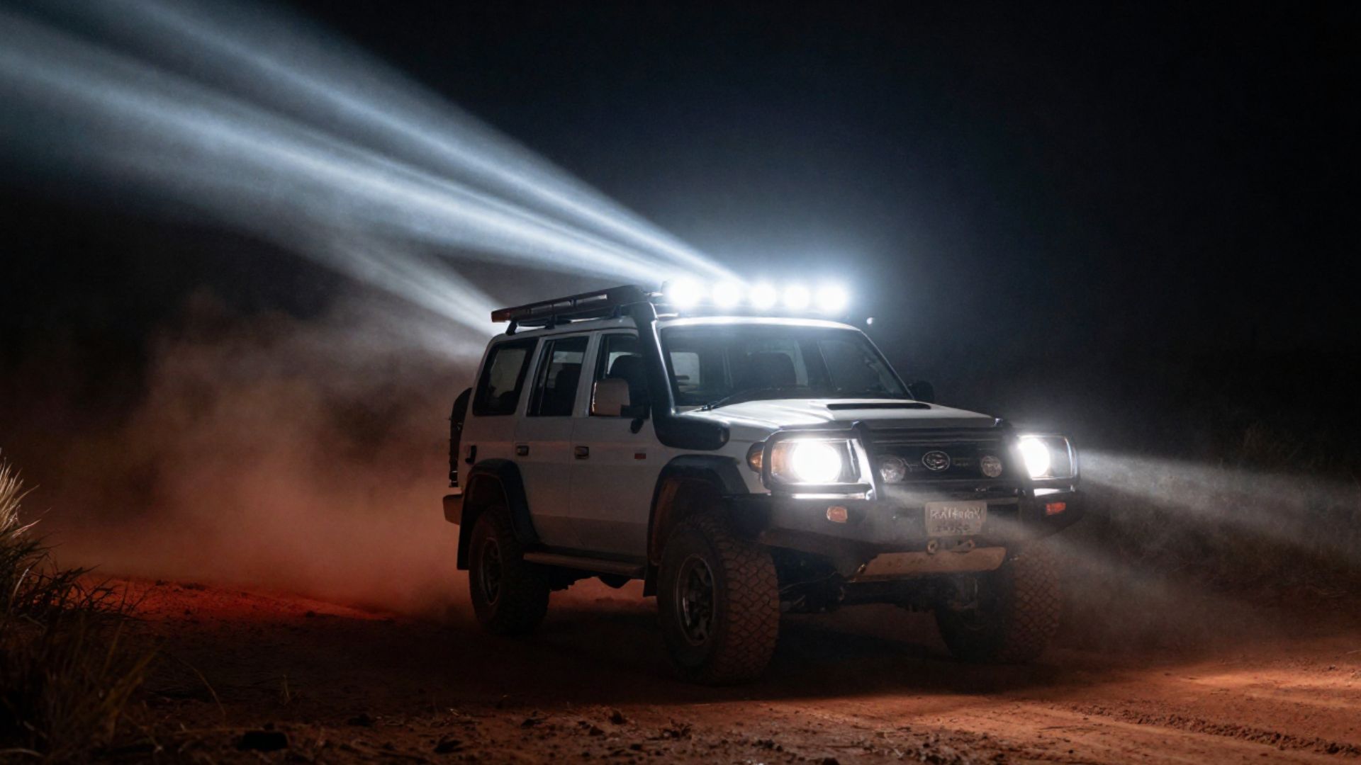 A 4WD on a dark bush track at night with driving lights blazing a long beam down the trail.
