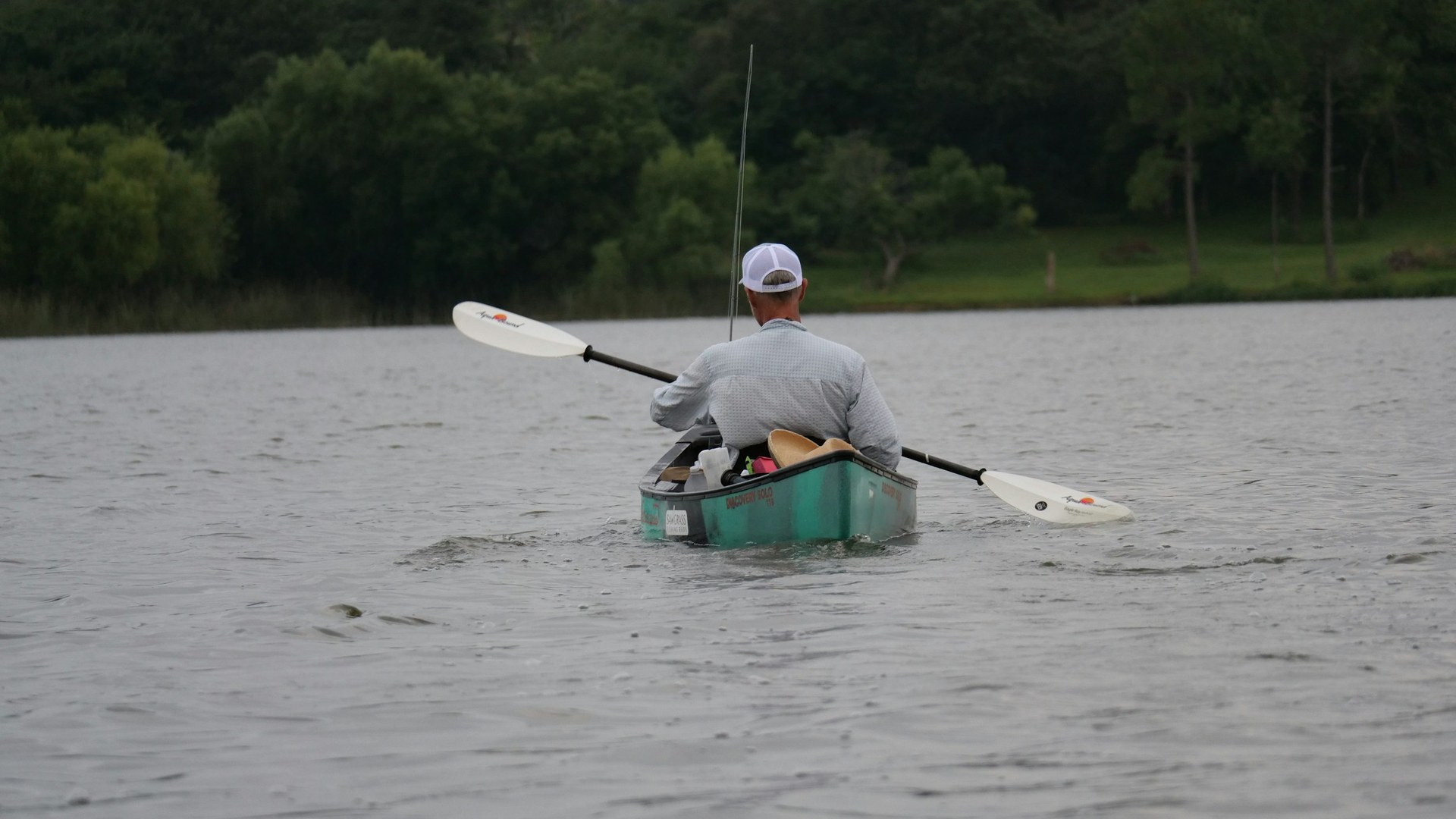 Angler paddling a fishing kayak on calm lake water