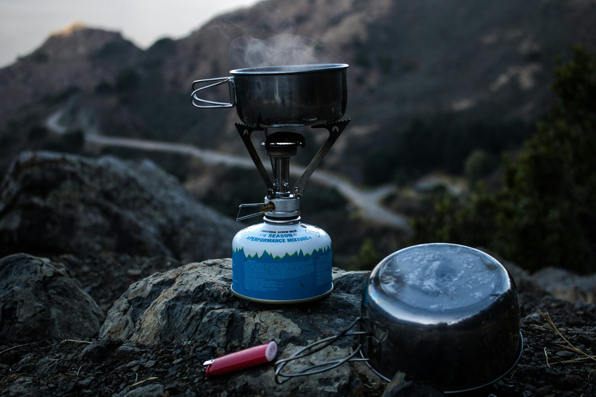 Compact camping stove and cookware set up on rocks in the mountains