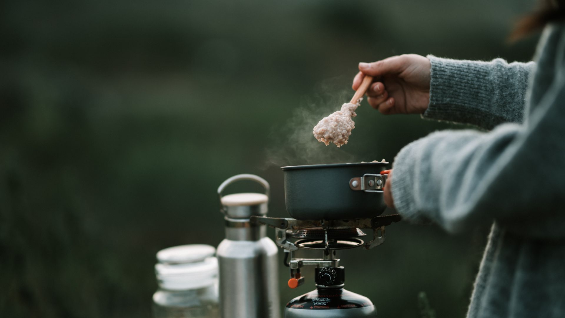 Camper cooking a meal on a compact portable stove at a campsite