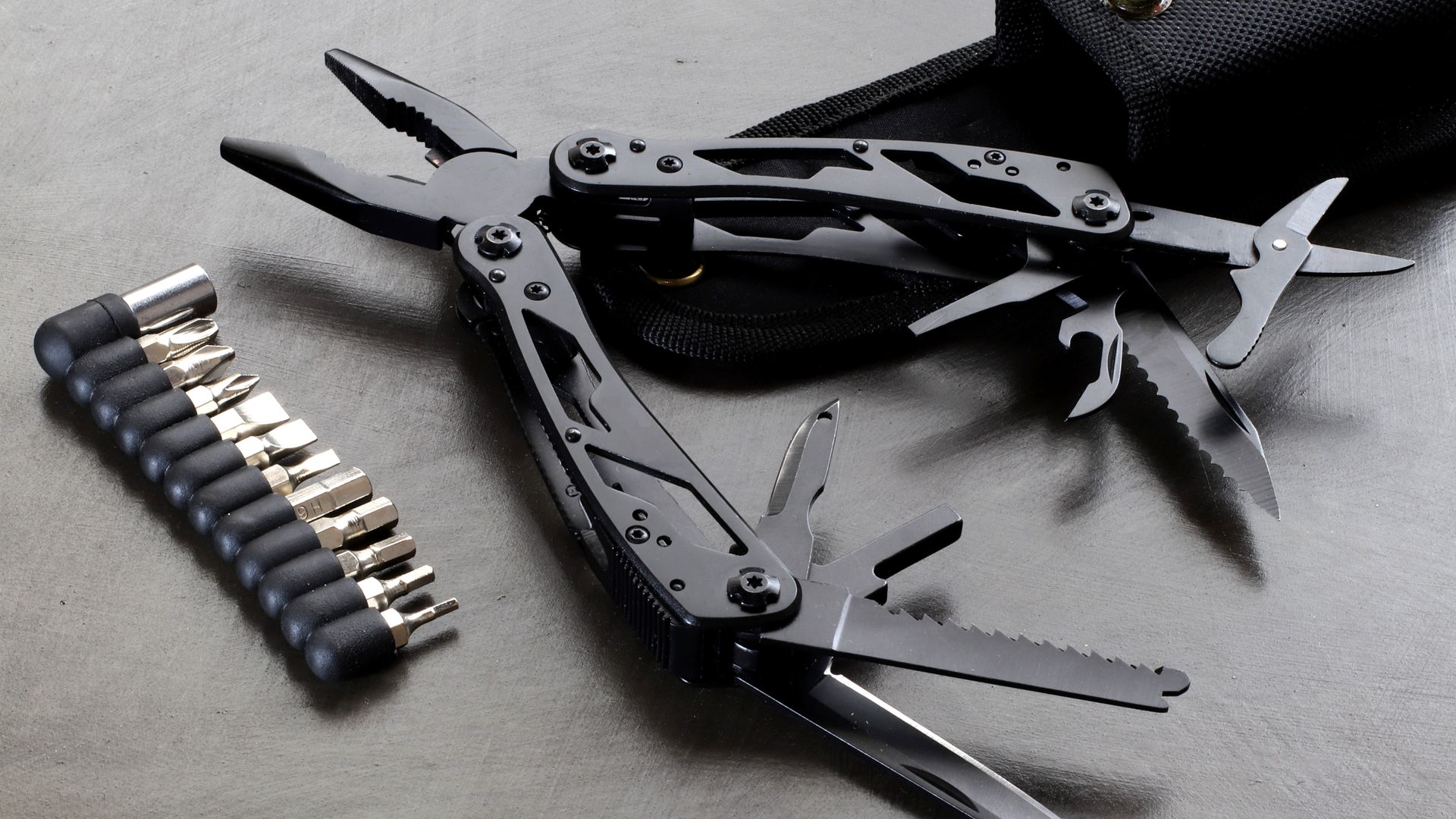Folding multi-tool opened with a set of screwdriver bits on a dark surface