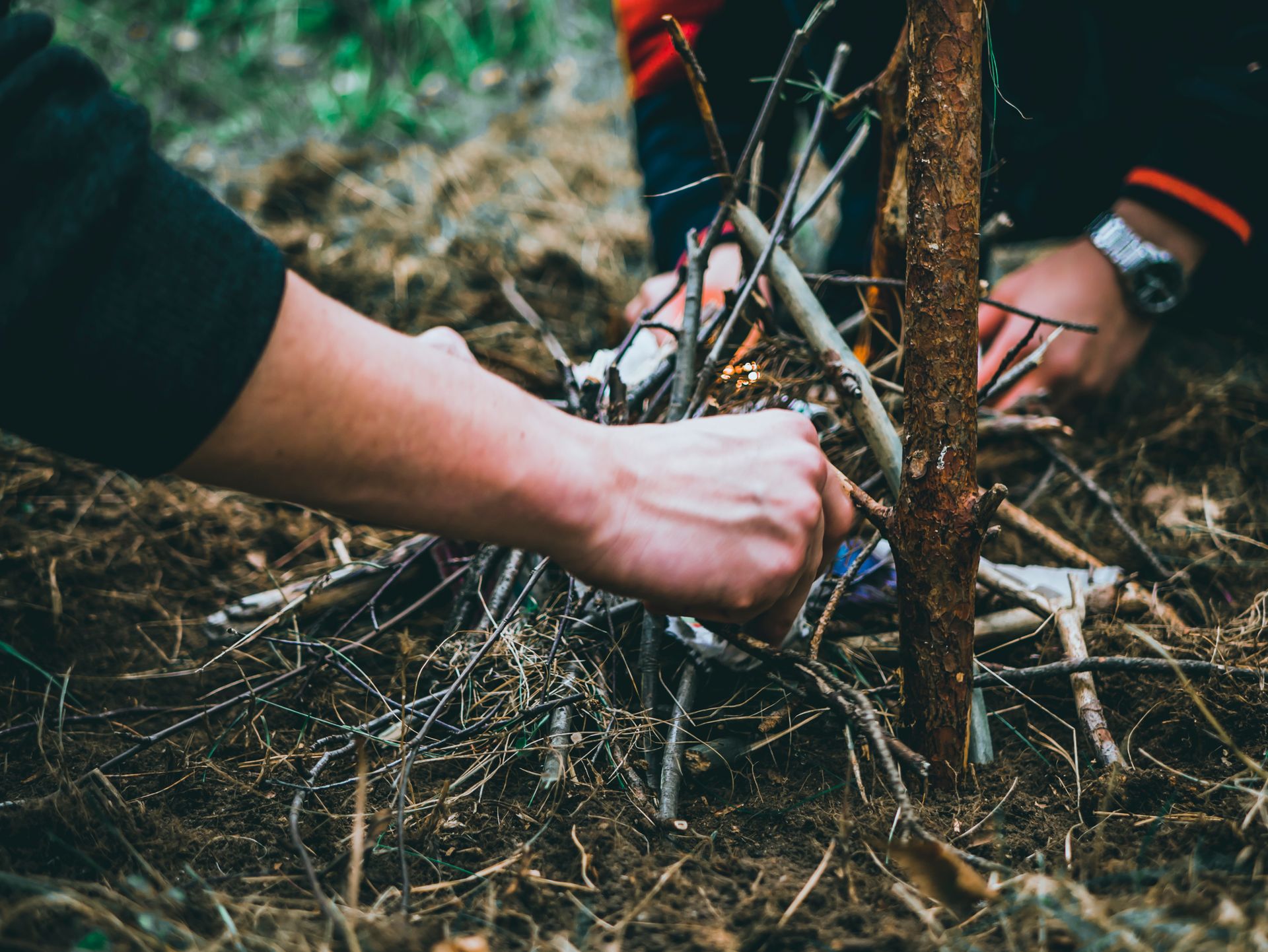 Hands arranging kindling and tinder to build a small fire at a campsite