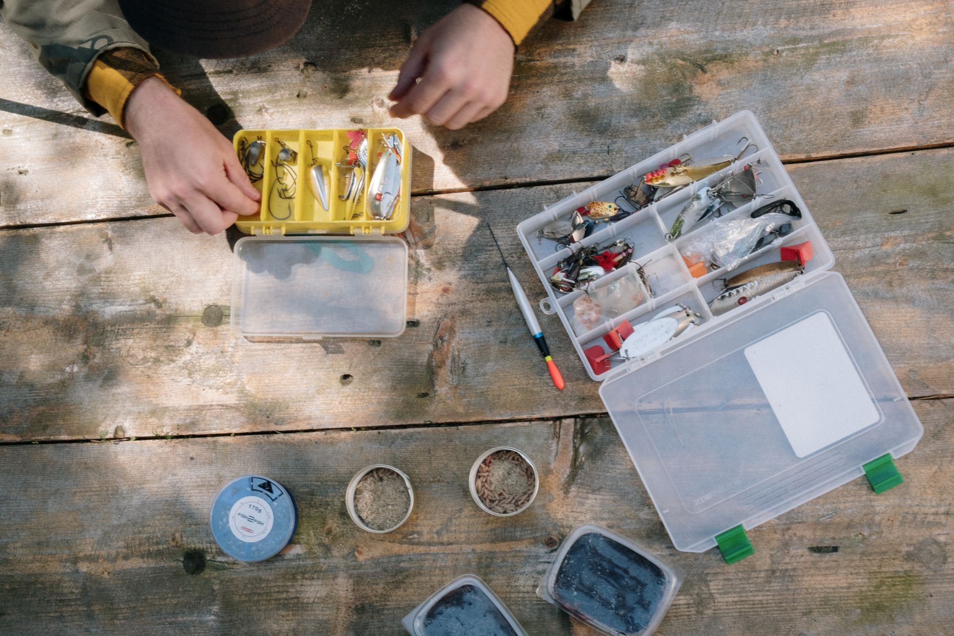 Fishing tackle boxes, tools and bait laid out on a rustic wooden surface