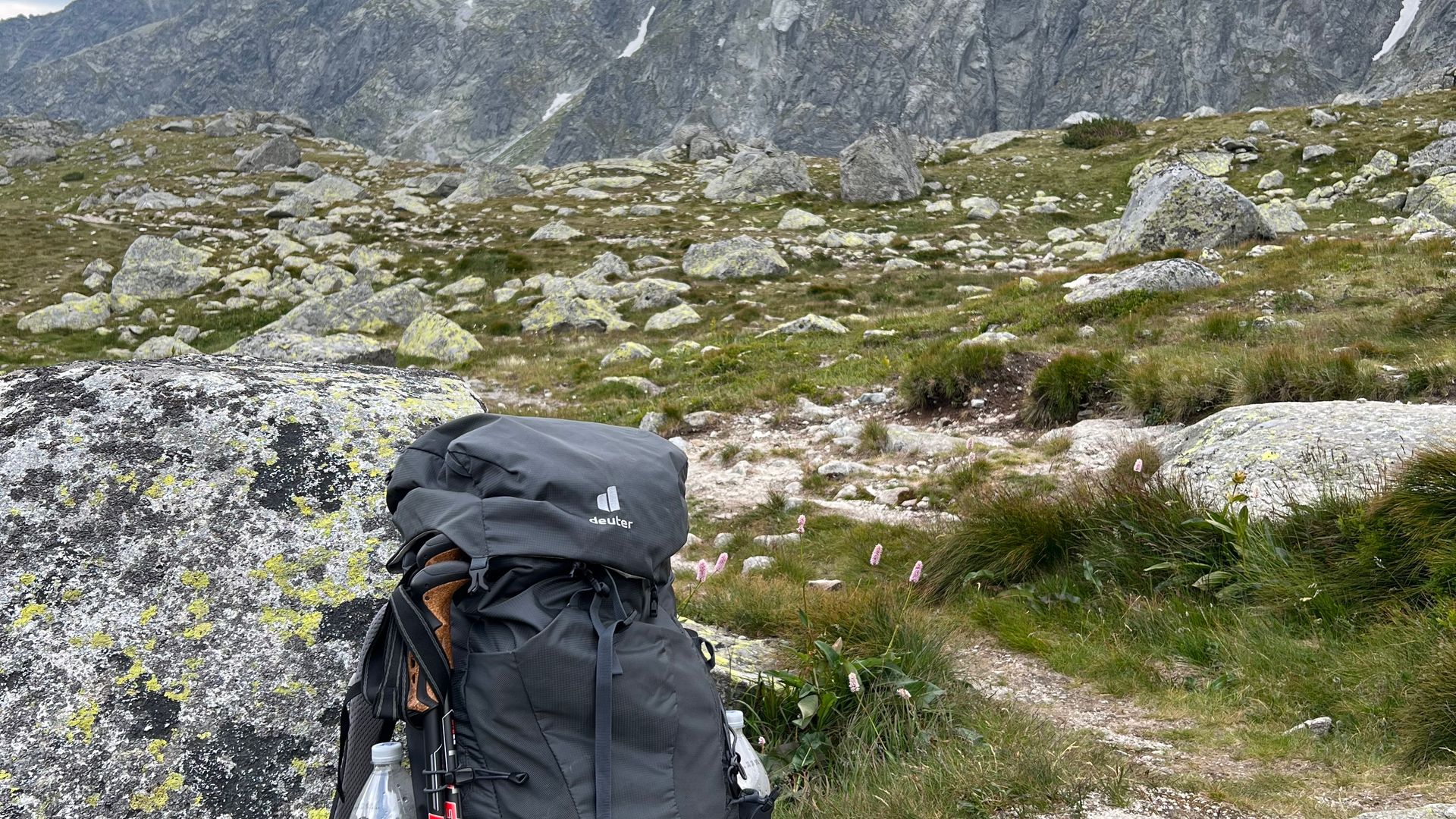 A hiking daypack resting on rocky mountain terrain beside a trail